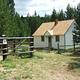 White cabin in meadow with rail fence and pine trees