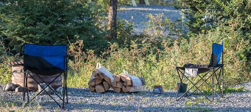 Campsite detail showing camp chairs, stacked firewood and a fire ring on a gravel pad — useful for illustrating campsite amenities and atmosphere; appears in the property image set.