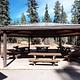 A metal ramada provides shade for picnic tables in a coniferous forest.