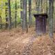 Small enclosed wooden pit toilet building. Surrounded by trees in late fall.