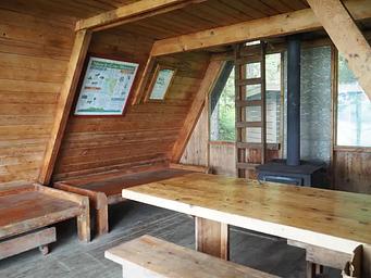 Interior of wood cabin showing 2 wood bunks, table, stove and ladder up to loft