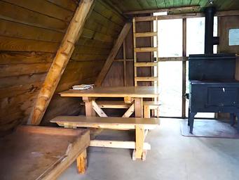 Mount Rynda Cabin interior showing wood table and bed with stove and ladder to loft