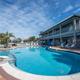 Outdoor swimming pool surrounded by lounge chairs and a two-story hotel building under a partly cloudy sky.