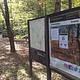 Bulletin board and map sign in the forest near a sidewalk and building in a campground