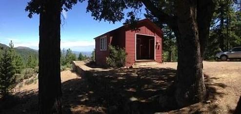Red cabin in between trees with blue sky in background.