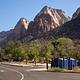 Recreational vehicle water fill and dump station with recycling and trash bins at the entrance to South Campground in Zion National Park, with dramatic sandstone cliffs rising in the background.