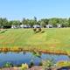 Panoramic hillside shot showing a line of RVs parked above a pond with landscaping and a covered picnic shelter — demonstrates campsite layout and grounds (from Amenities page).