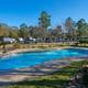 Clear daytime photo of the resort-style swimming pool with fenced area and RV sites visible in the background — matches the park amenities and appears on the park homepage gallery.