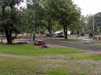 Small photo of a grassed campsite area with picnic table, fire ring and adjacent paved pad — useful close-up of a typical campsite. Found on the About / Camping Rates context (about.html), supporting relevance to the property.