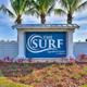 Entrance sign photo with 'The Surf' branding, landscaping and palms — establishes property identity and arrival experience (gallery / site signage image).