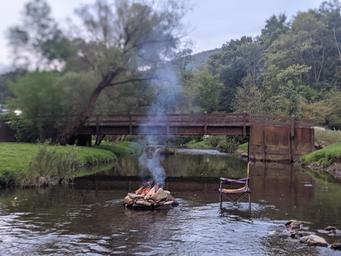 Small campfire ring in the creek with a wooden bridge in background — highlights creek access, rustic features and scenic water setting on the property (page: Facilities).