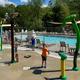 Pool and splash pad with children playing and the adjacent pool visible — clearly shows on-site aquatic recreation facilities (slide image on site highlighting pool/splash area).