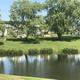 Shoreline view showing trees, grassy campsites and RVs across the pond — highlights campsite character and landscaping (Overview/gallery image).