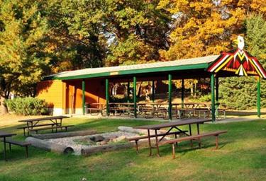 Covered picnic pavilion with multiple picnic tables and a central firepit area — shows group picnic/amenity space featured on the campground’s page.