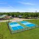Aerial view of two blue tennis courts beside a grassy field and small building under a clear sky