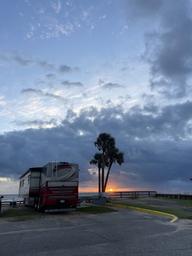 Sunset scene showing an RV parked near the sea wall and a section of the grounds — captures atmosphere, RV parking, and waterfront setting (social/gallery image on the site).