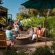 Family gathered around a paved fire pit adjacent to an RV, with landscaping and site furnishings visible — a facilities/amenity shot from the campground's own photo set.