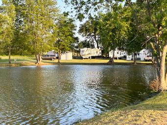 Pond with RV sites visible across the water: shows wetland edge, water reflections and RVs in the background — useful to illustrate campsite views and lakeside pitches (Activities/gallery).