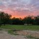Scenic sunset view over grassy area and trees on the property — useful for conveying the park’s landscape and ambiance (featured as homepage/social image).