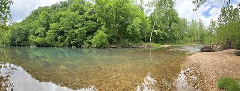 A view of Little Piney Creek, waterway in front with green vegatation in the background