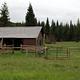 Cabin with red siding and fences in flat meadow backed by conifer forest
