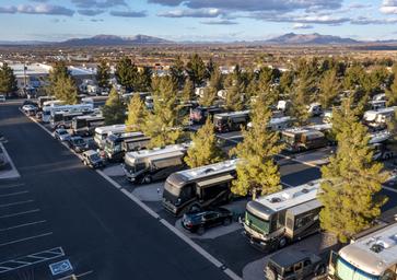 Elevated/drone view of multiple RVs parked in designated paved sites with trees and mountains in background — identifies typical RV pitch arrangement (DJI_0196-copy).