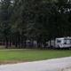 Photo of RVs and campsites among trees with picnic tables and gravel road — shows typical site/RV pitch setup; sourced from About page content about the campground.