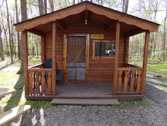 Exterior of a rustic cabin labeled with a name plate, front porch and picnic table — good for showing cabin rentals (source: Cabins / Rental page).