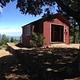 Red cabin in between trees with blue sky in background.