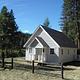 White cabin in meadow with split rail fence and pine trees