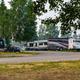 Wide banner view showing a row of parked RVs at the site with grassy foreground and trees — useful campsite/RV pitch scene demonstrating layout and unit size.