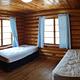 Log cabin bedroom with two twin beds log walls, wood floors and windows with blue drapes. 
