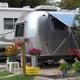 Close view of two RVs on a site with awning, potted plants and site utilities visible — useful for showing site detail and campsite amenities (source: homepage/news images).