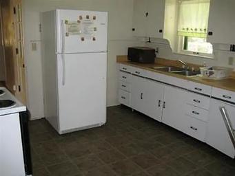 Kitchen with full size fridge with upper freezer, microwave next to metal sink with dish rack across from electric stove.
