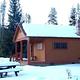 Thick snow covers a wooden cabin and picnic table.