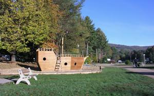 Playground feature shaped like a pirate ship on a grassy area with surrounding campground roads and trees — useful amenity shot from the property gallery.