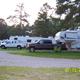 Row of RVs and pull-through sites with trucks visible on gravel pads and tree-lined background — clearly shows typical RV camping spaces at this KOA (from 'Ways to Stay' imagery).