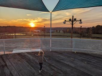 Wide deck/view at sunset with shade sails and park grounds visible — good overview of an elevated amenity and surrounding landscape.