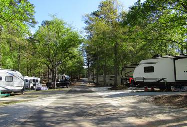 View down a campsite road flanked by RVs and trees — good overall view of RV site layout and wooded campground environment (appears on the campground's listing).