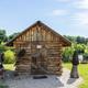 Small rustic log cabin on a grassy lakeshore with carved wooden sculptures nearby — clearly shows on-site cabin and waterfront setting (homepage imagery).
