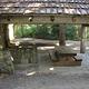 Cascadian style pole shelter protecting picnic table next to stone fireplace and chimney.