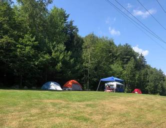 Open grassy tent field with multiple tents and tree line — shows tent camping area and site layout (Tent page).