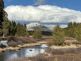 Bunsen Peak under cumulus clouds with a creek in the foreground. The trailhead for Bunsen Peak is not far from Indian Creek Campground