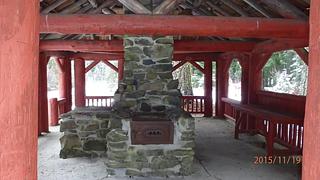 Stone fireplace and chimney next to counter under red-painted log shelter.