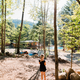 Tree-lined campsite/recreation area with a child in the foreground and site structures visible — useful for showing family-friendly wooded grounds and play/amenity areas.