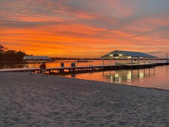 Sunset view of the sandy beach and main dock/pier with covered structure — good scenic shot of the campground waterfront and beach area (from the site homepage).