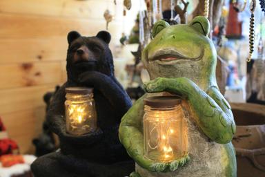 Close-up of decorative frog and bear lantern figures inside a wooded interior — likely from the campground’s on-site store or office gift area (visible on the property home page, shows on-site amenities/merchandise).