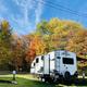 Large fifth-wheel RV on a maintained grassy site with clear sky and tree line — good representation of full-hookup RV sites on the property (IMG_5823 from the gallery).