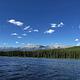 A photo of Lake Alva on a sunny day. The water and skies are bright blue, and trees and the swan range can be seen in the background.