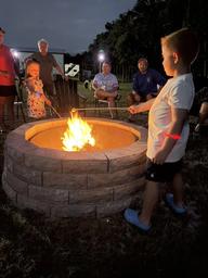 Nighttime scene of a stone fire pit with guests (children/adults) gathered — shows a communal amenity and guest experience on the property.